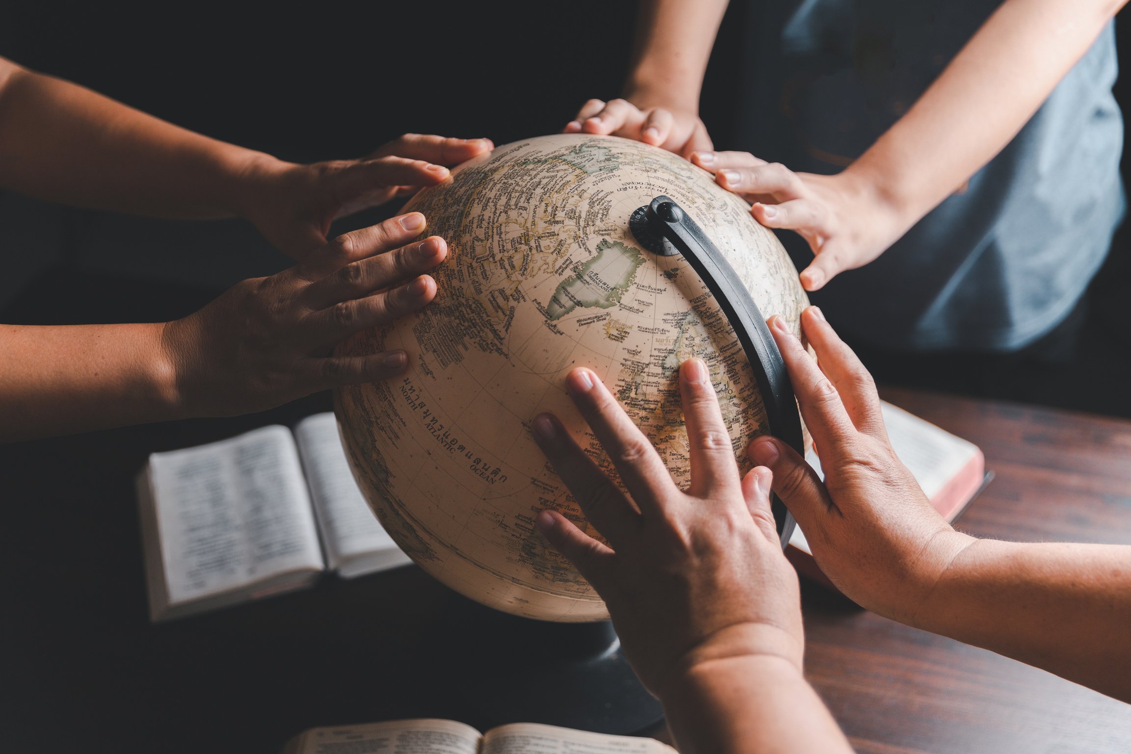 Christian group praying for globe and people around the world on wooden table with bible. Christian small group praying together around a wooden table with bible page in homeroom.